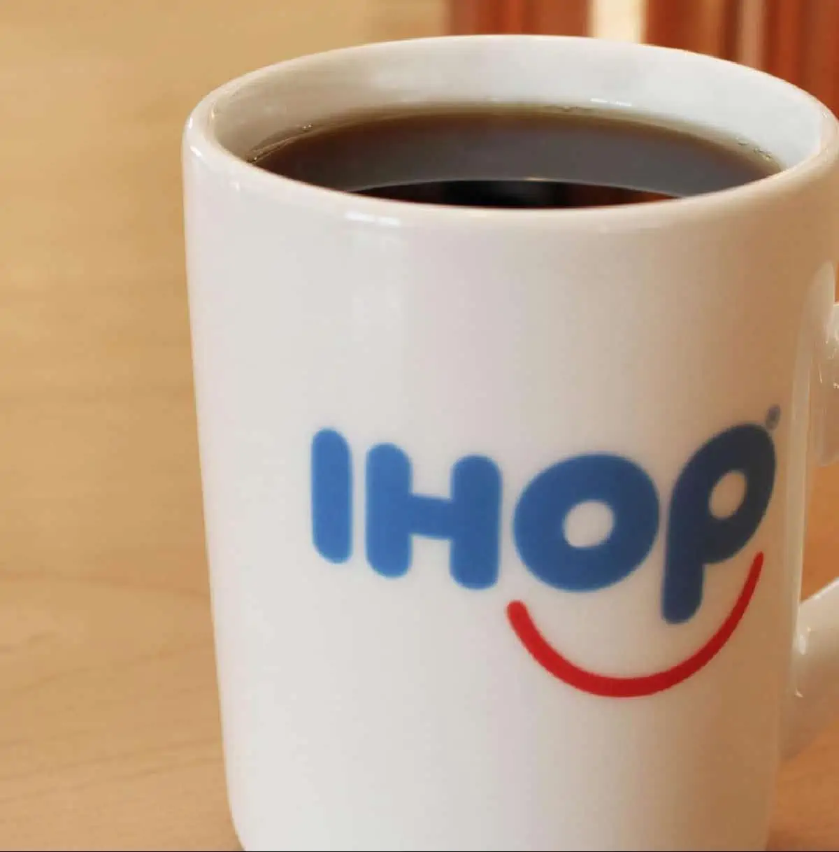 A large mug of hot coffee in a white IHOP mug with logo in blue and red. 