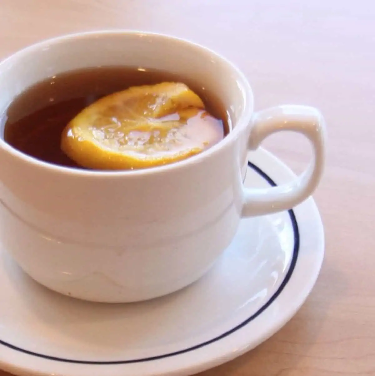 A cup of IHOP hot tea with a slice of lemon in a white cup and saucer on a countertop. 