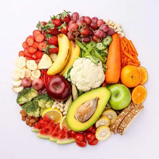 A variety of fruits, vegetables, legumes, whole grains and nuts shaped into a circle on a light background.