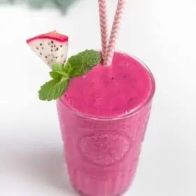Bright Pink Dragon Fruit Smoothie served in a glass with a slice of pitaya and sprig of mint.