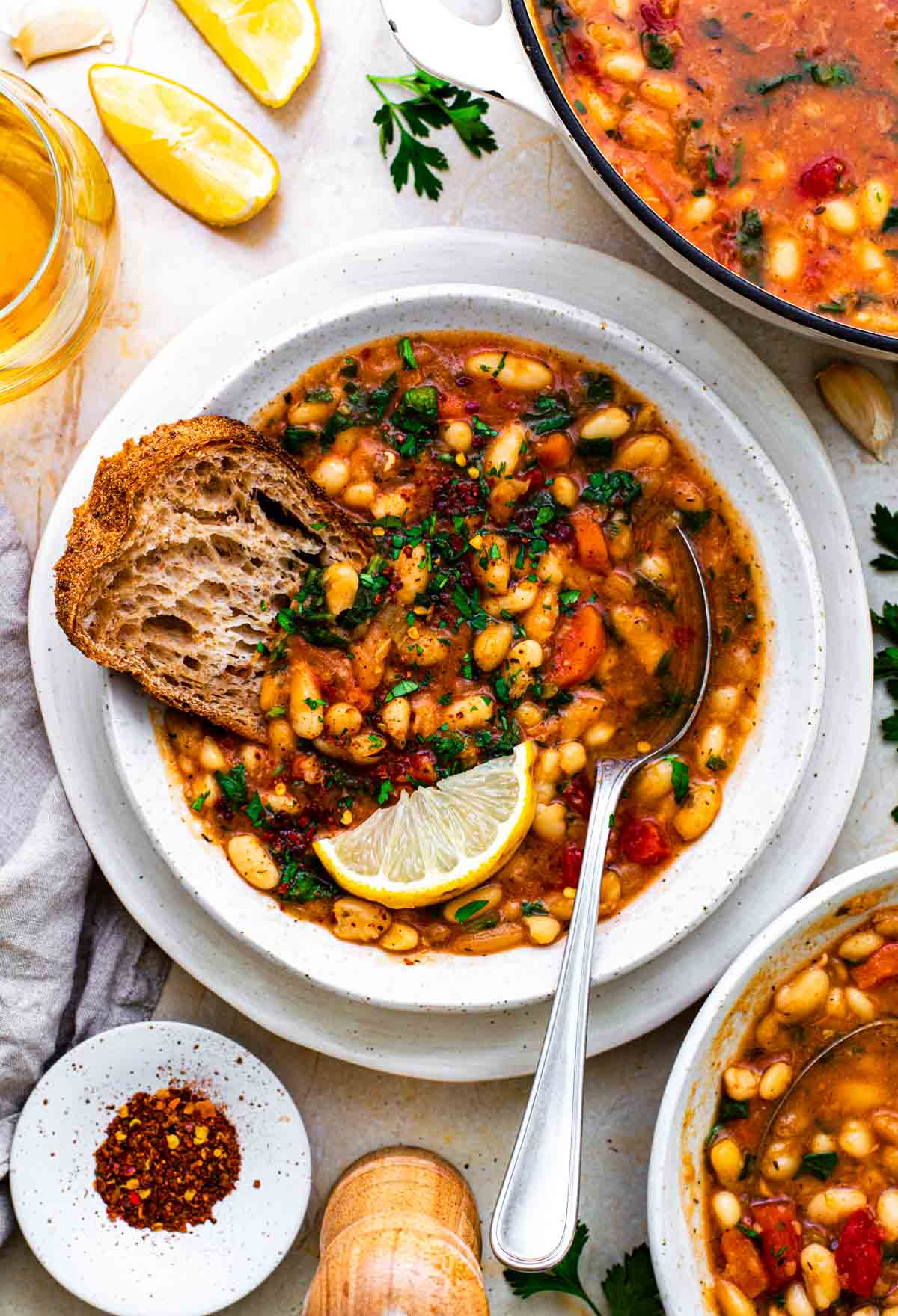 Navy bean vegetable soup in a white bowl with carrots, greens, and sourdough bread. 