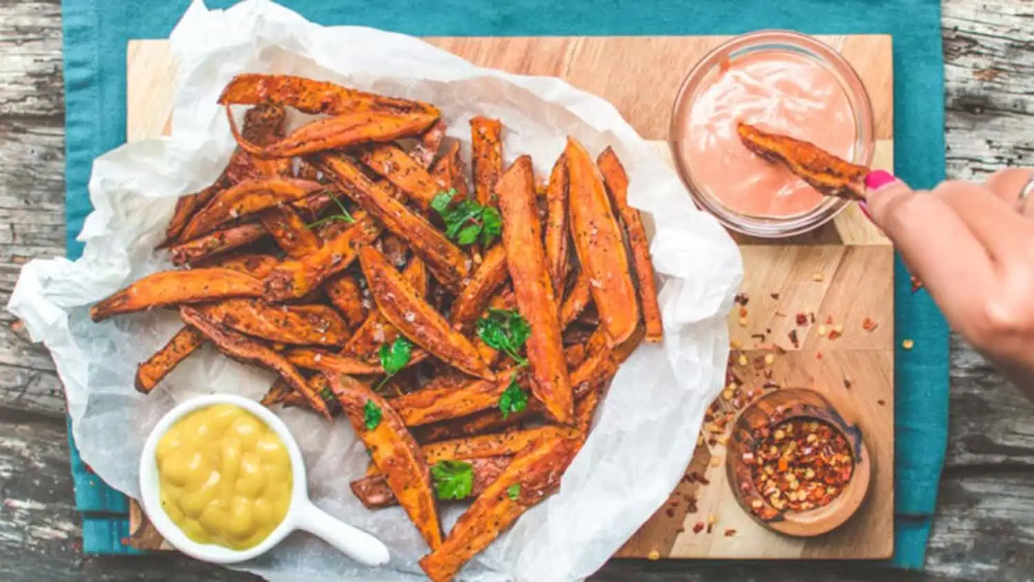 plate of sweet potato fries with a side of mustard and a hand dipping a fry into special sauce in the upper right-hand corner