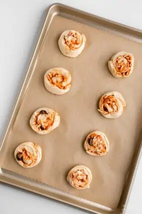 PIzza rolls on a parchment paper lined baking sheet about to go into the oven. 