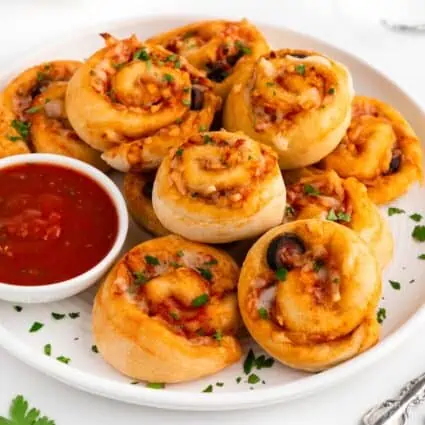 Vegan pizza rolls stacked on a white plate with marinara sauce.