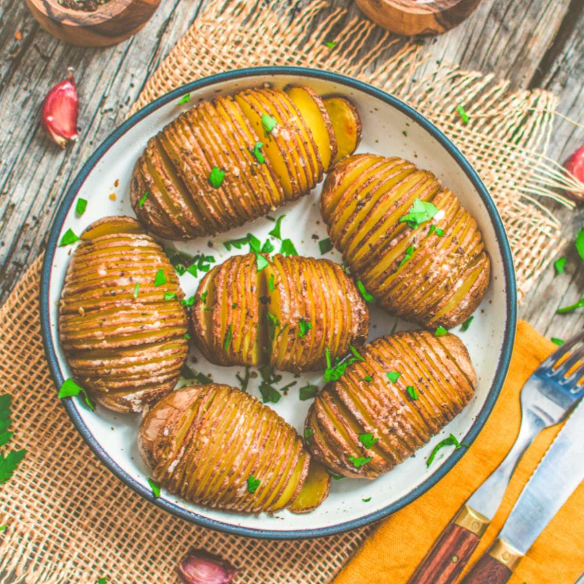 Vegan potatoes, Hasselback style, served on a platter with chopped herbs.