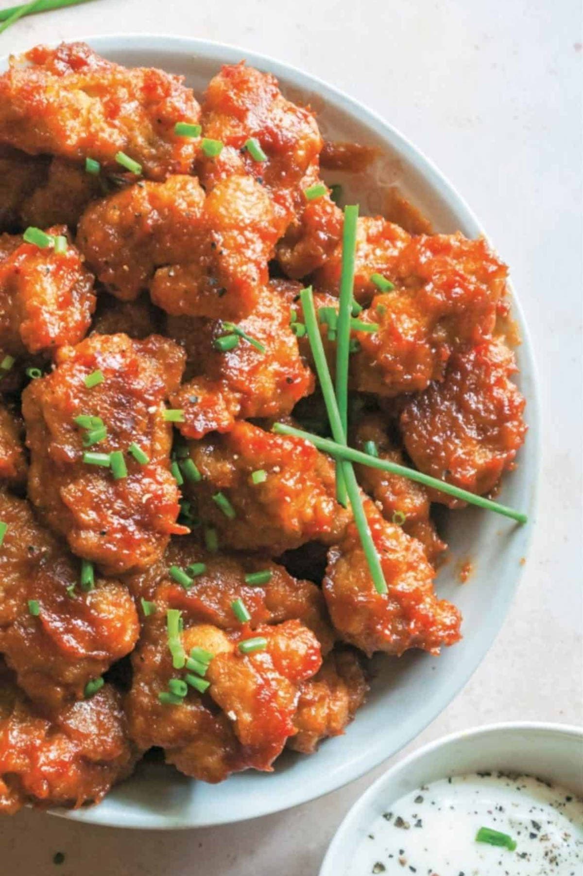 BBQ seitan wings piled on a platter with sliced chives on top.