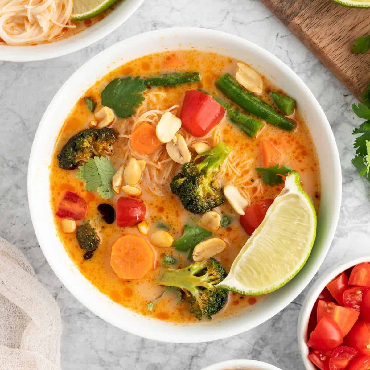 A bowl of Thai curry in a white bowl, garnished with a lime wedge.