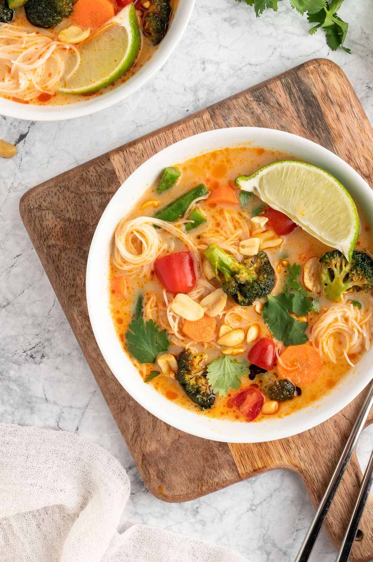 Thai curry in a white bowl on a wooden serving board against a marble background.