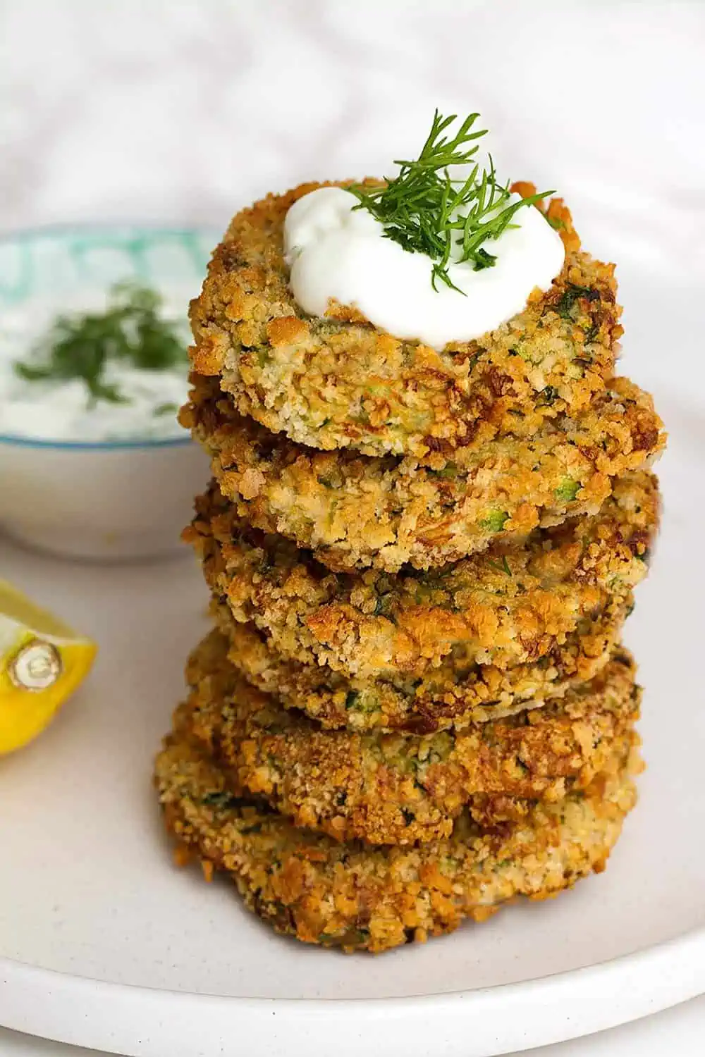a stack of air fried zucchini fritters topped with vegan cream and dill on a plate