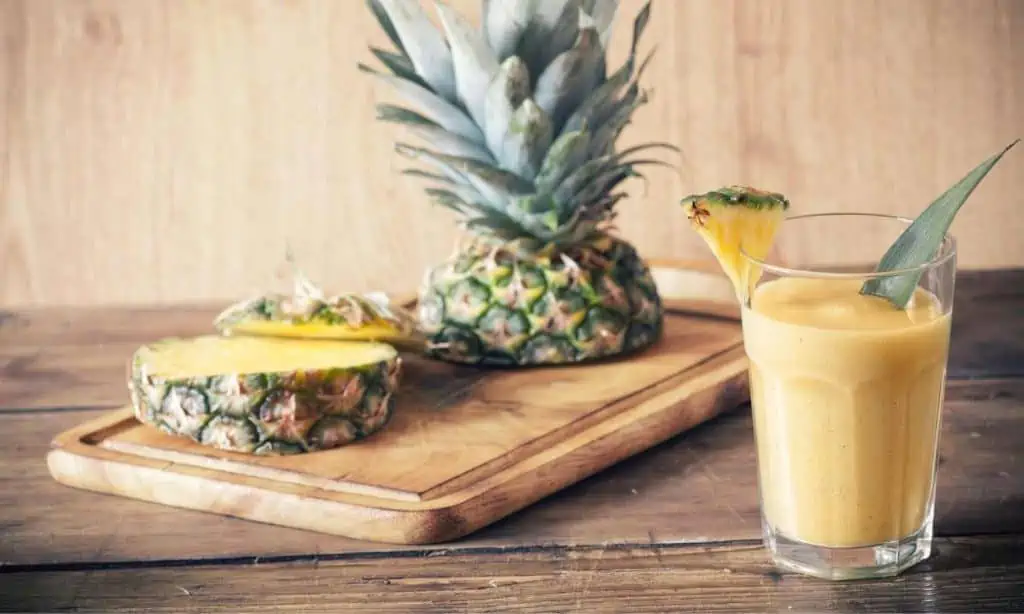 creamy vegan dairy-free pineapple smoothie next to a cutting board with a fresh sliced pineapple on it