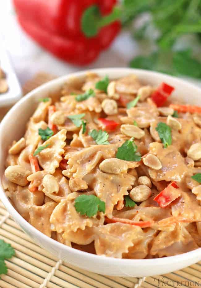 bowl of red curry bow tie pasta garnished with red bell peppers, cilantro, and peanuts