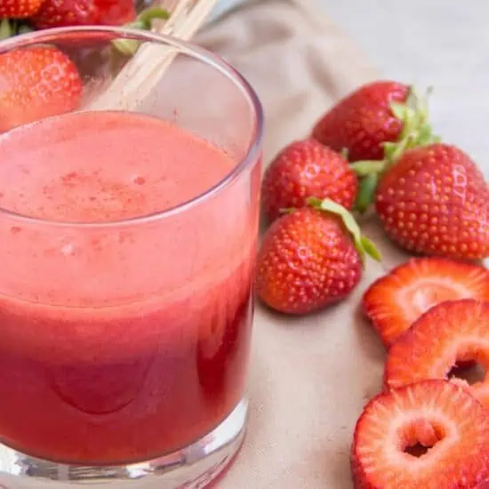 fresh strawberry juice served in a glass surrounded by ripe strawberries on a table