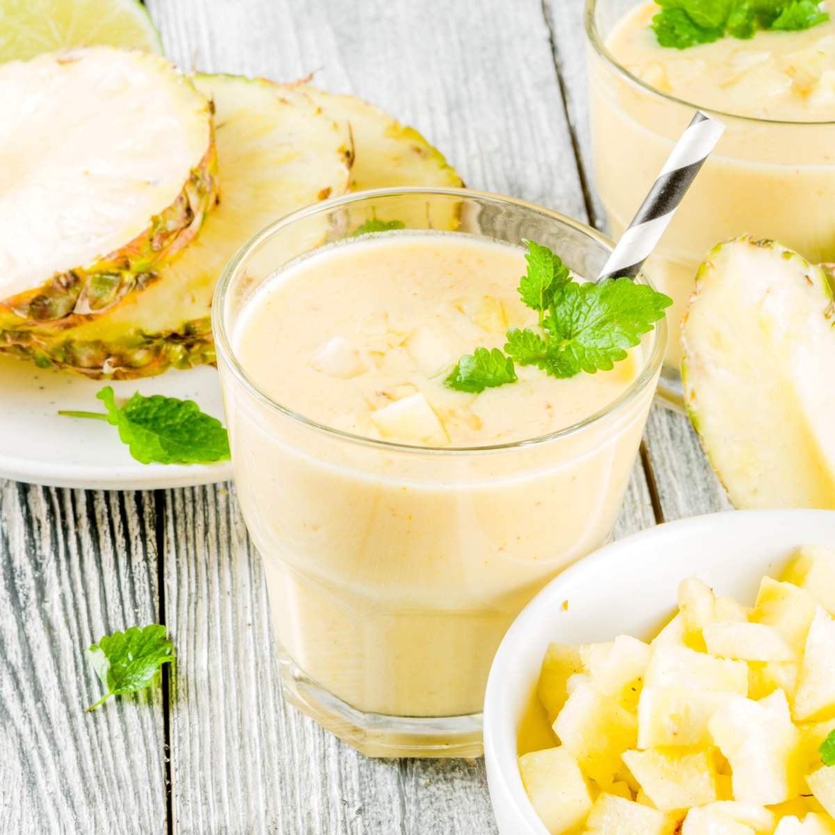 Pineapple banana smoothie in a small glass, next to a bowl of chopped pineapple.