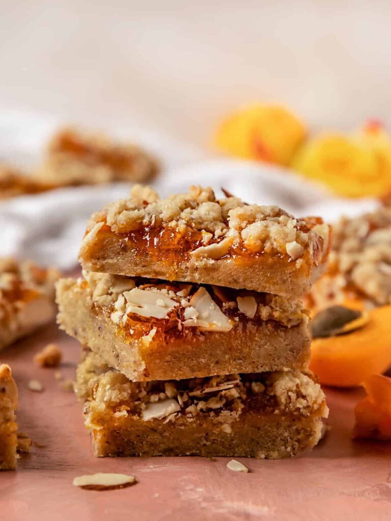 vegan apricot crumble dessert bars stacked up on a pink table