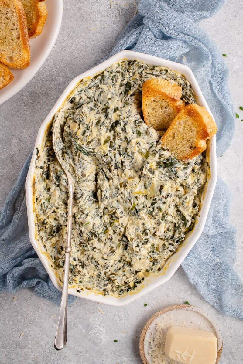 vegan artichoke dip in a casserole dish with toasted bread pieces