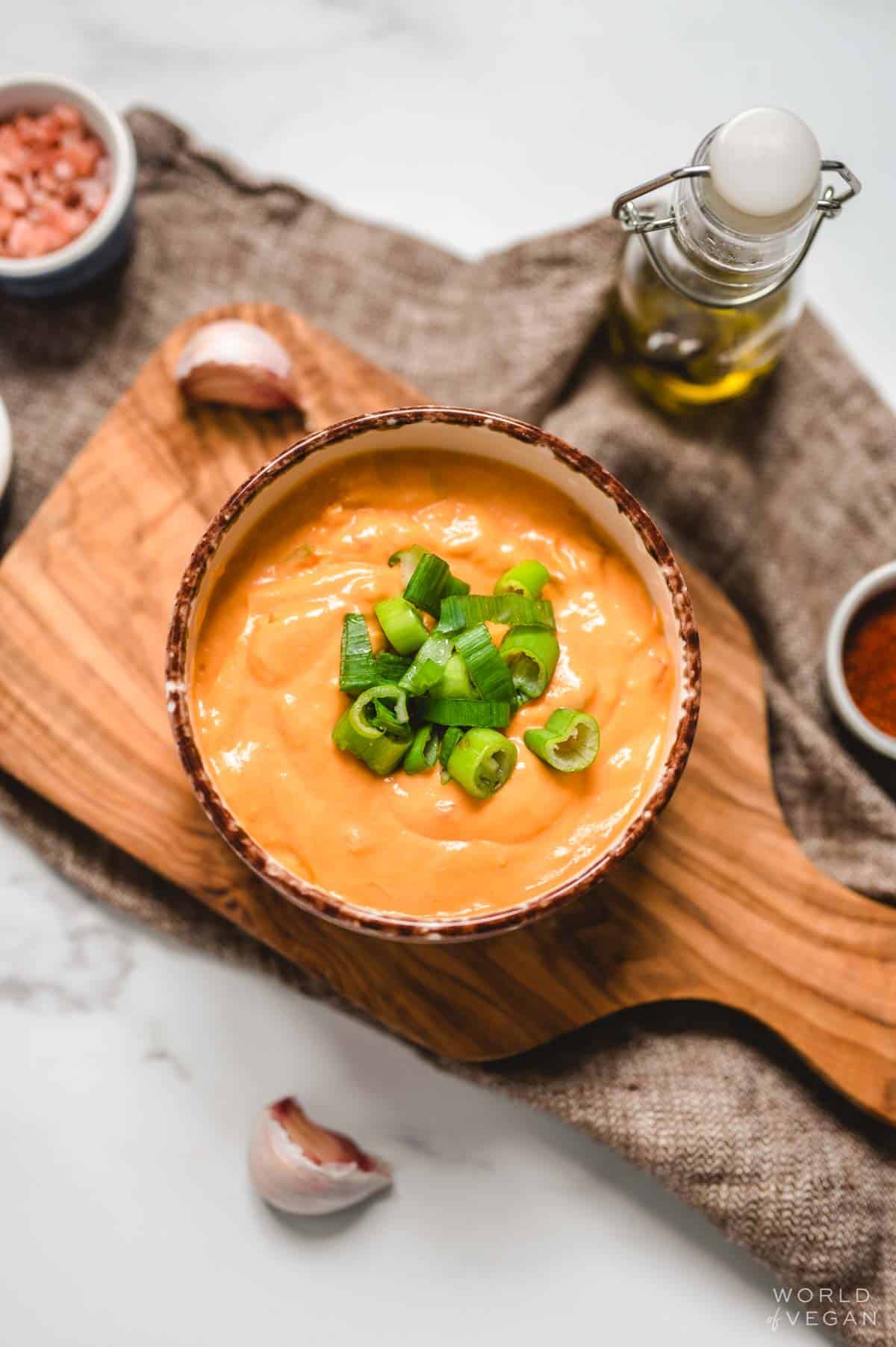 vegan buffalo queso dip in a serving bowl topped with green onion