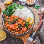 Vegan chickpea stew with tomatoes and spinach served in a bowl with rice, parsley, and lemon wedges.