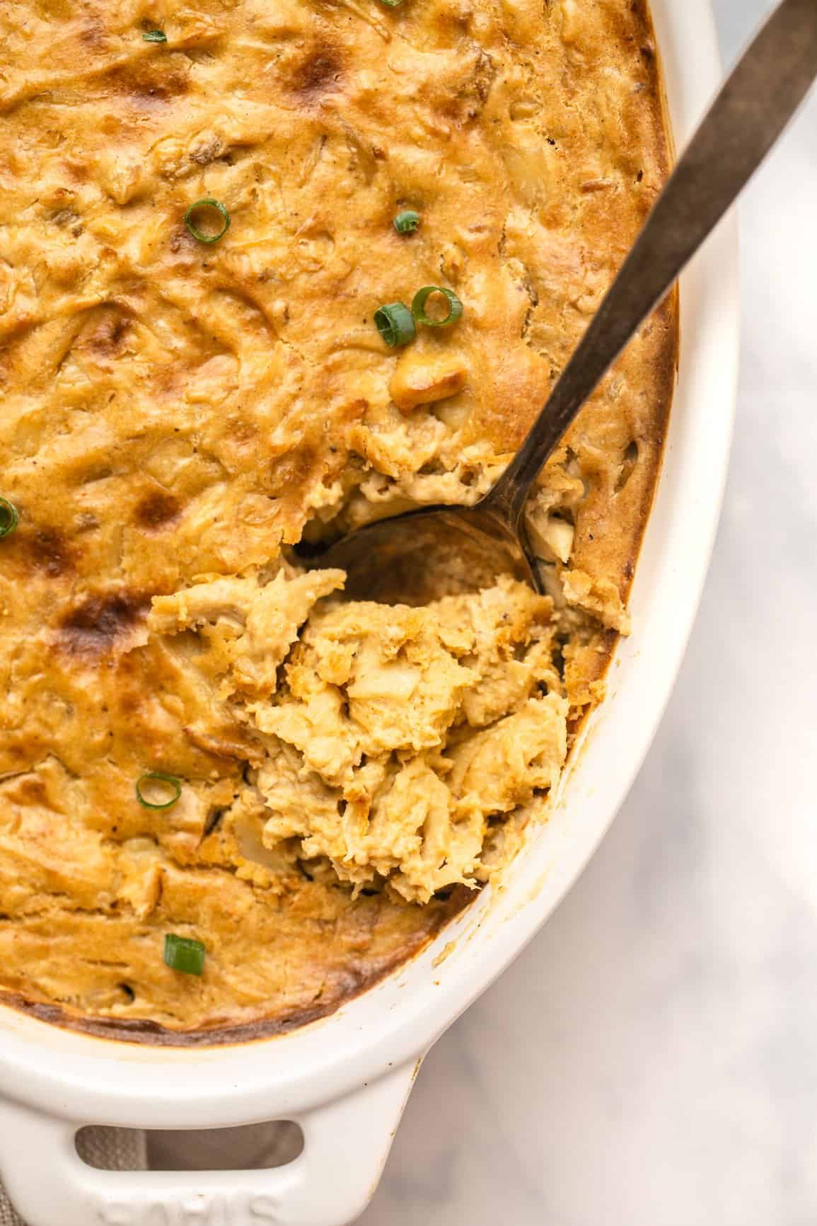 vegan crab dip in a white casserole dish with a spoon stuck into it