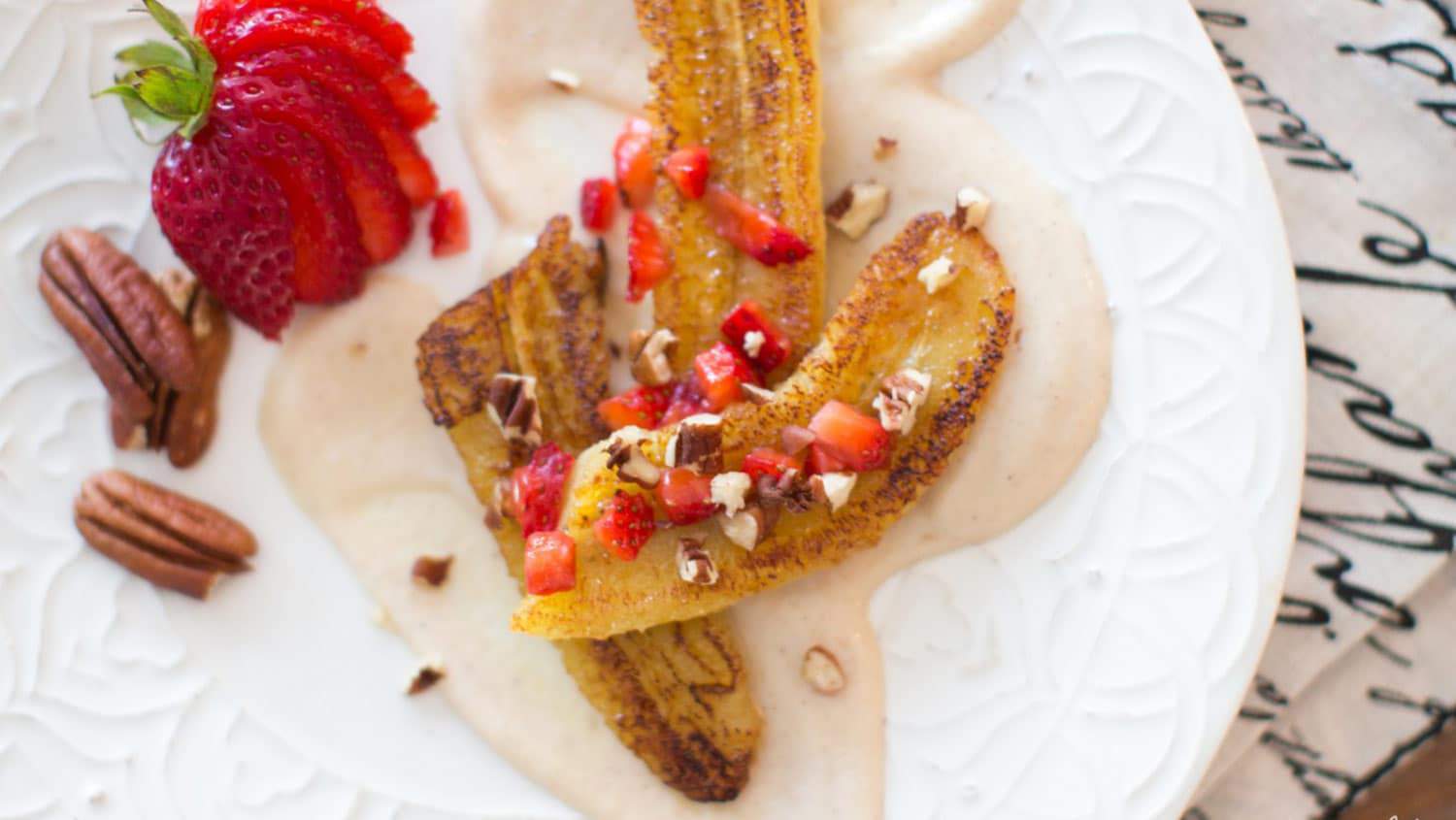 caramelized bananas with vegan cream sauce on a plate with sliced strawberries and pecans
