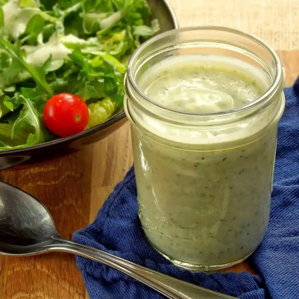 jar of homemade vegan ranch dressing next to a bowl of salad