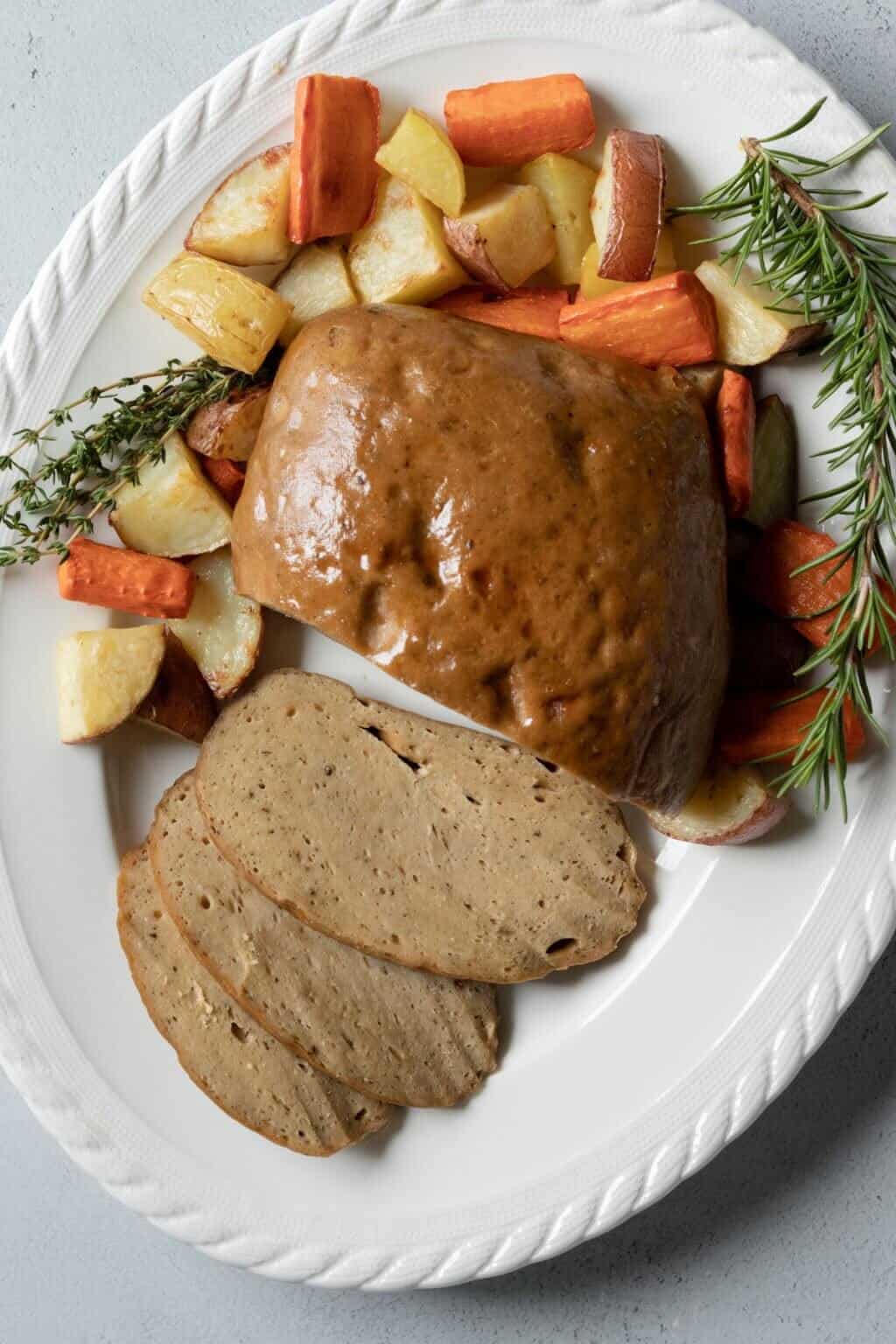 vegan turkey roast on a plate with roasted vegetables and herb garnish