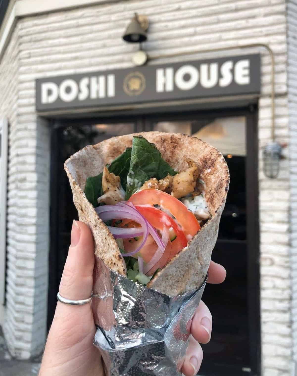 A hand holding a vegan gyro near the entrance of the Doshi House in Houston, Texas.
