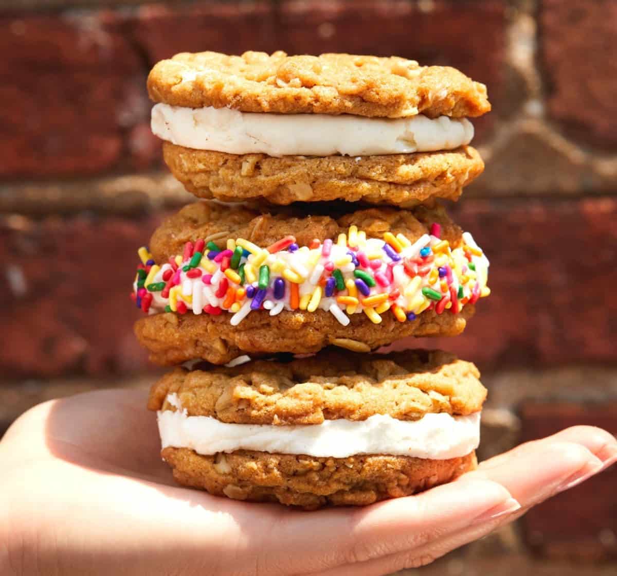 Hand holding a stack of oatmeal cookies filled with vegan buttercream frosting.