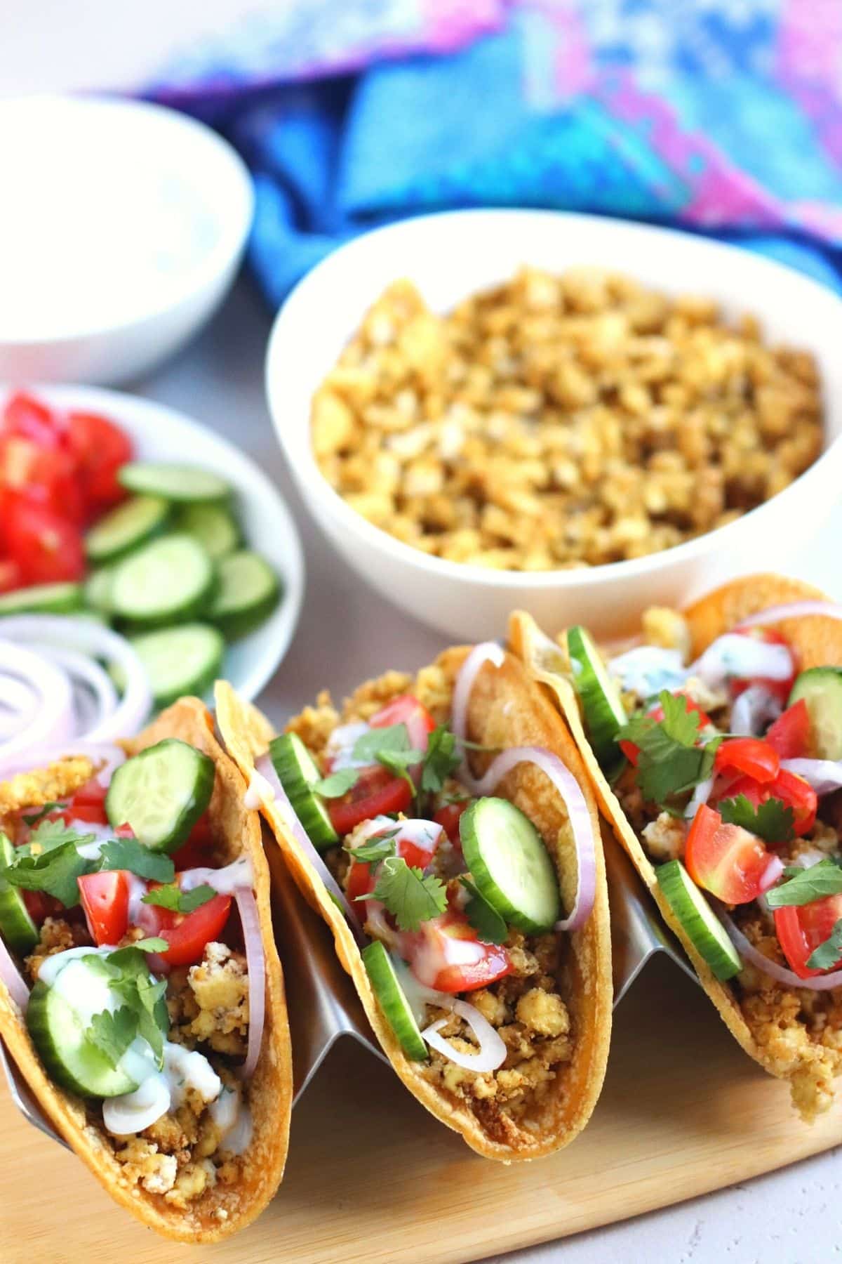 Three hard taco shells filled with crumbled tofu, red onion, cucumber, tomatoes, and a vegan yogurt sauce.