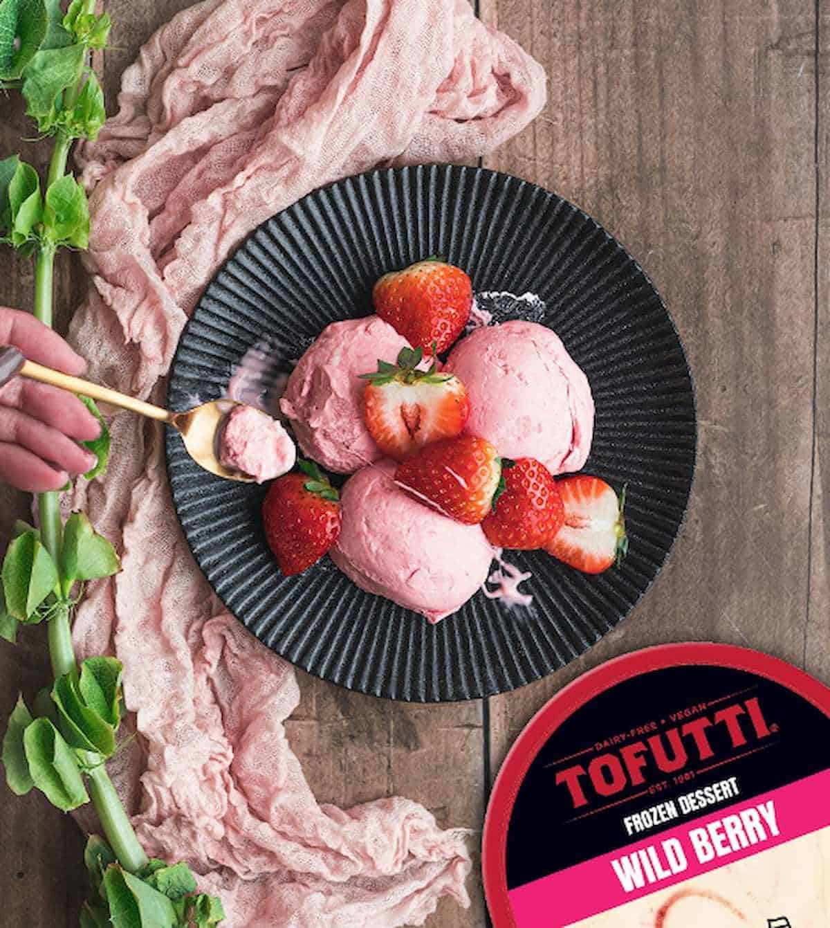 Hand with spoon scooping into a bowl of Tofutti wild berry frozen dessert.