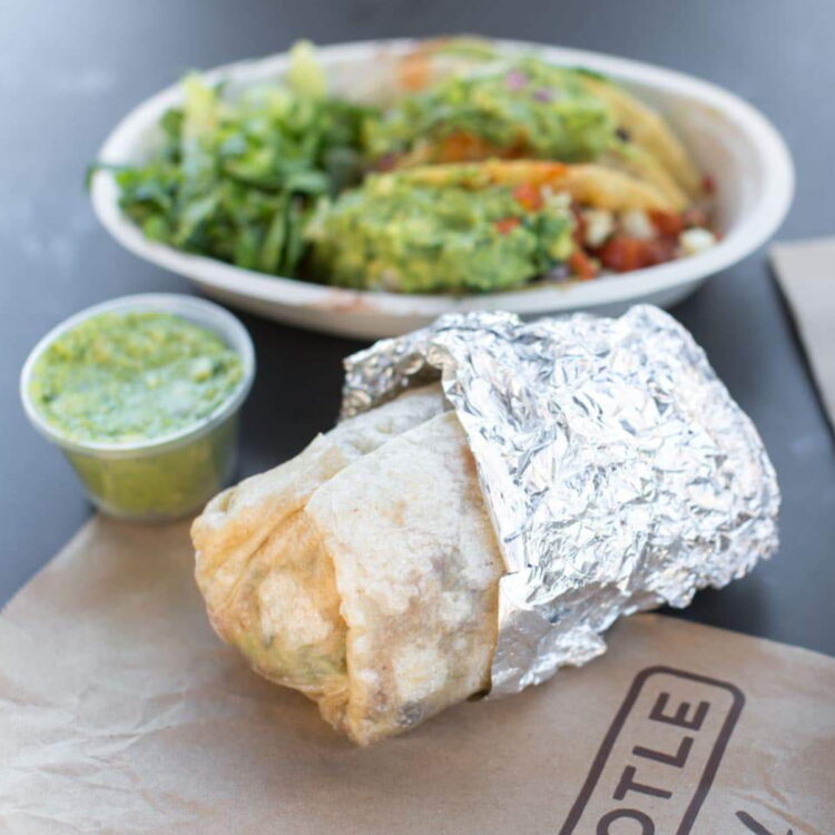 A veggie burrito bowl beside a burrito and a side of guacamole.