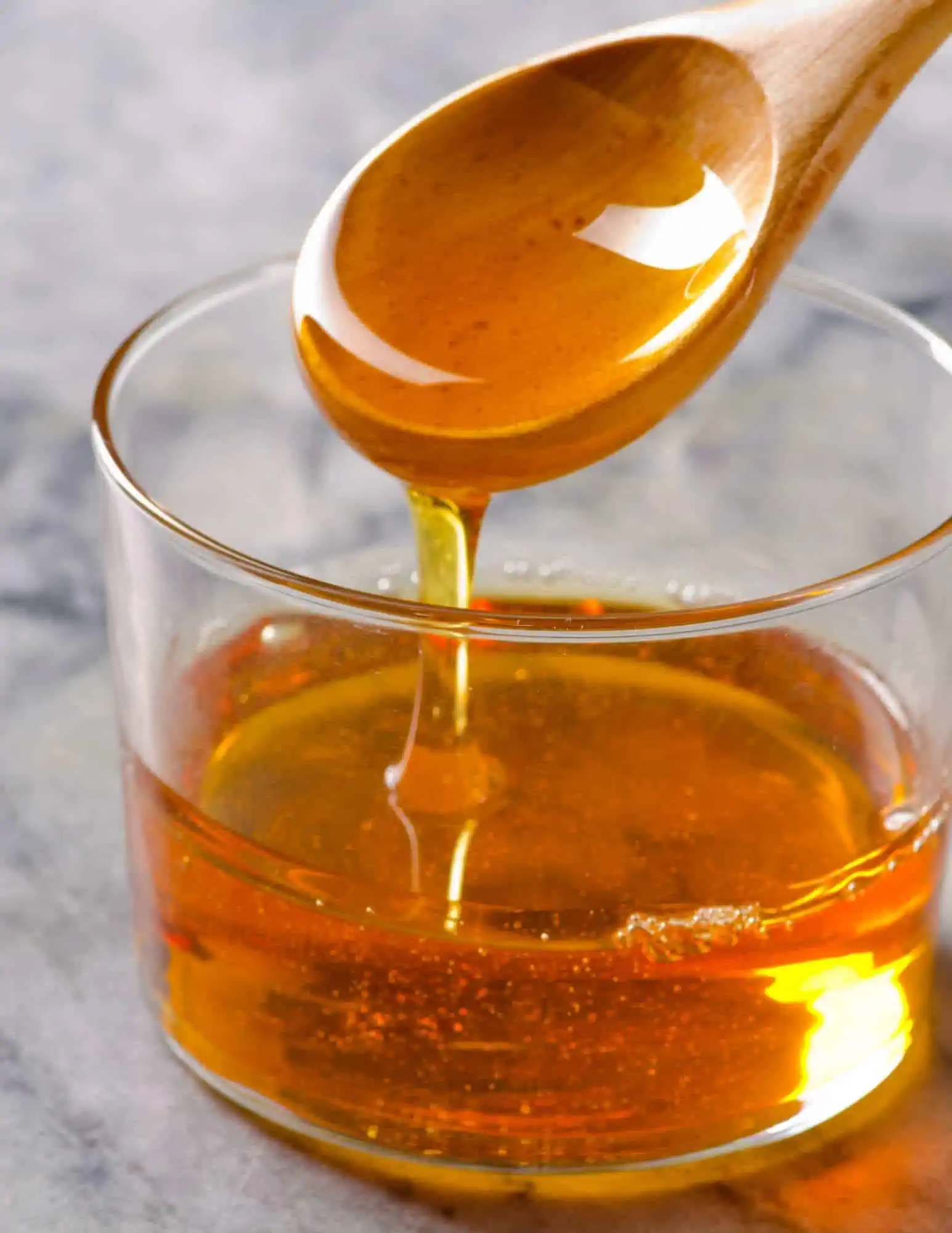 Agave nectar dripping off a spoon into a glass jar.