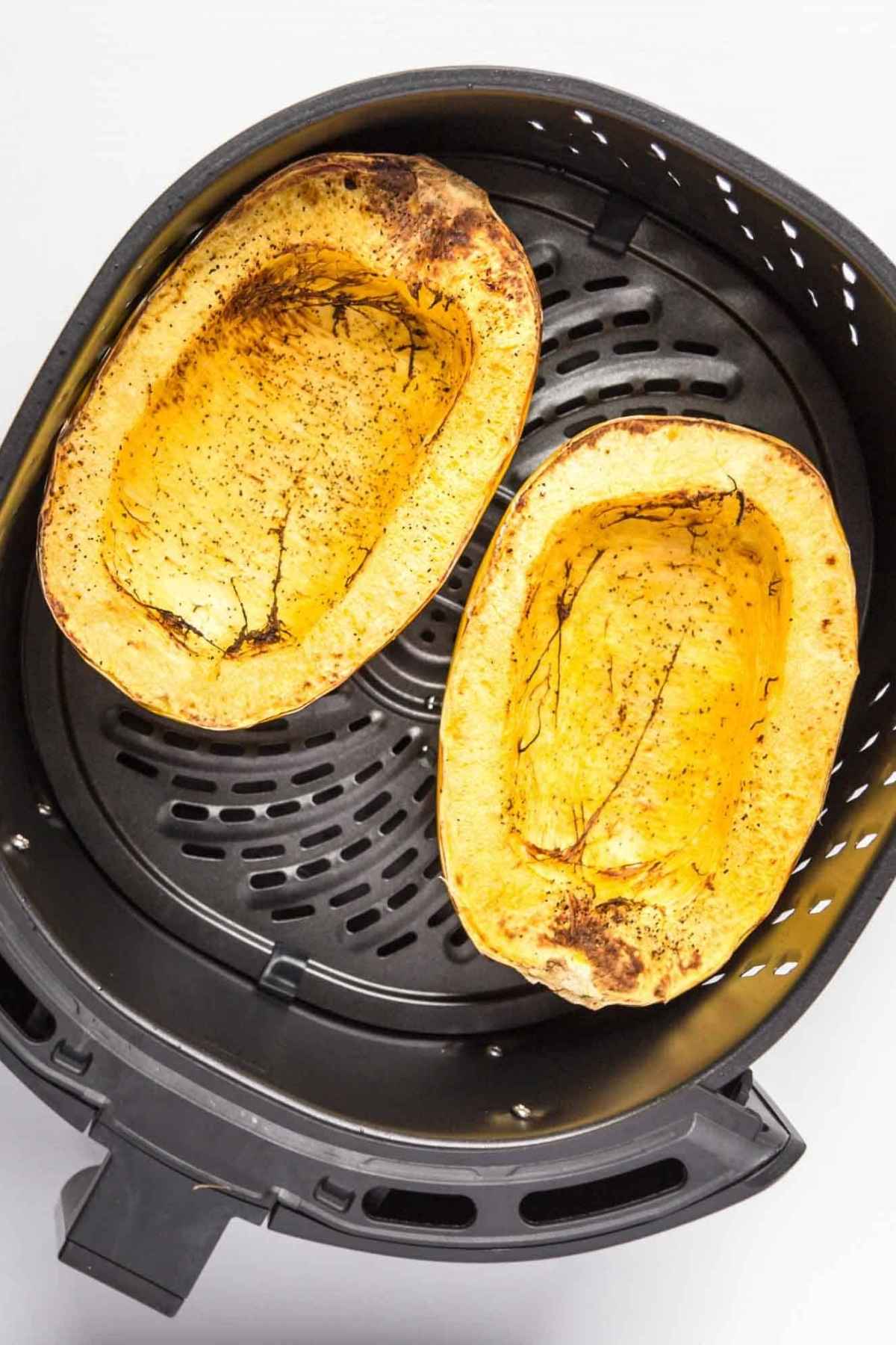 Halved squash in an air fryer with caramelized edges.