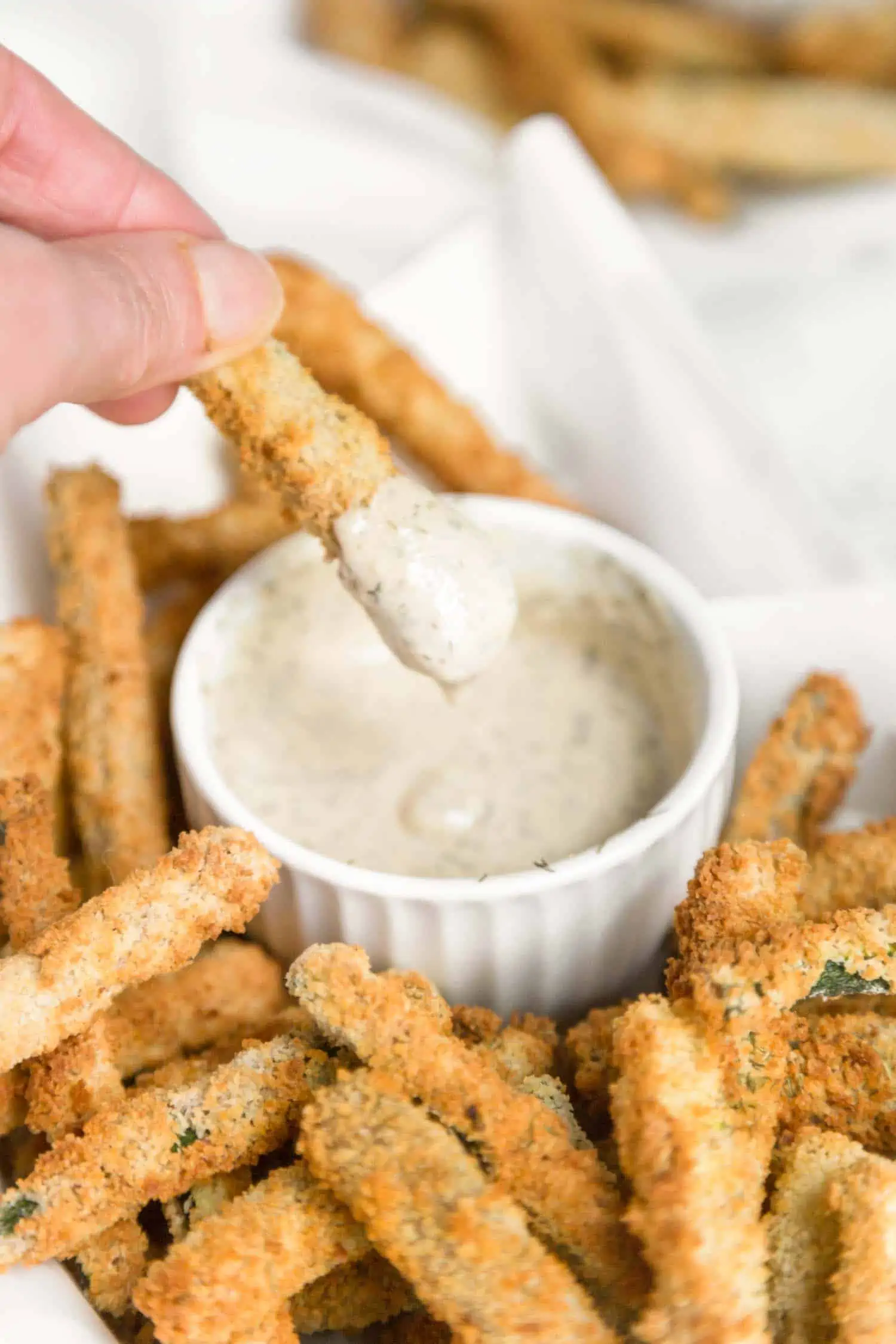 Hand holding a zucchini fry and dipping it into a creamy sauce.