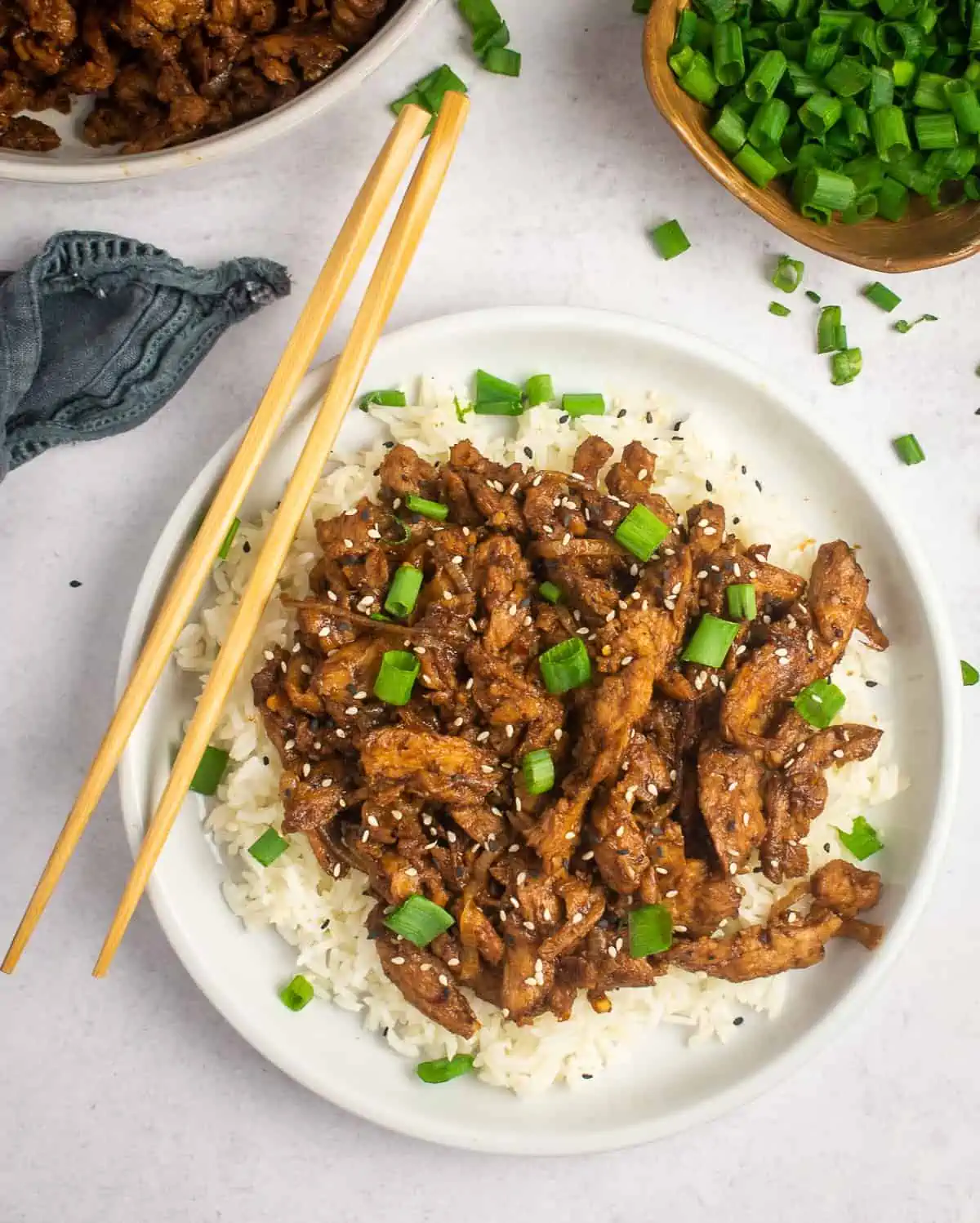 vegan bulgogi on a plate over white rice with chopsticks on the left side and scallion garnish