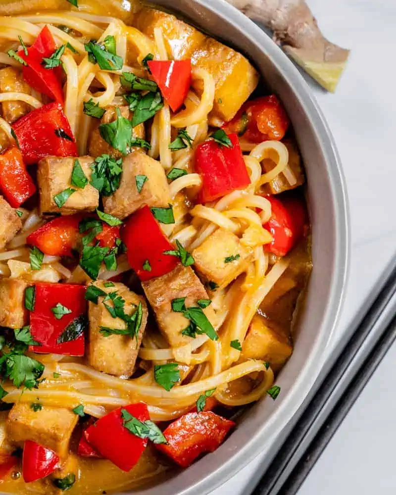 bowl full of noodles, tofu, bell peppers, and herbs in a garlic ginger broth