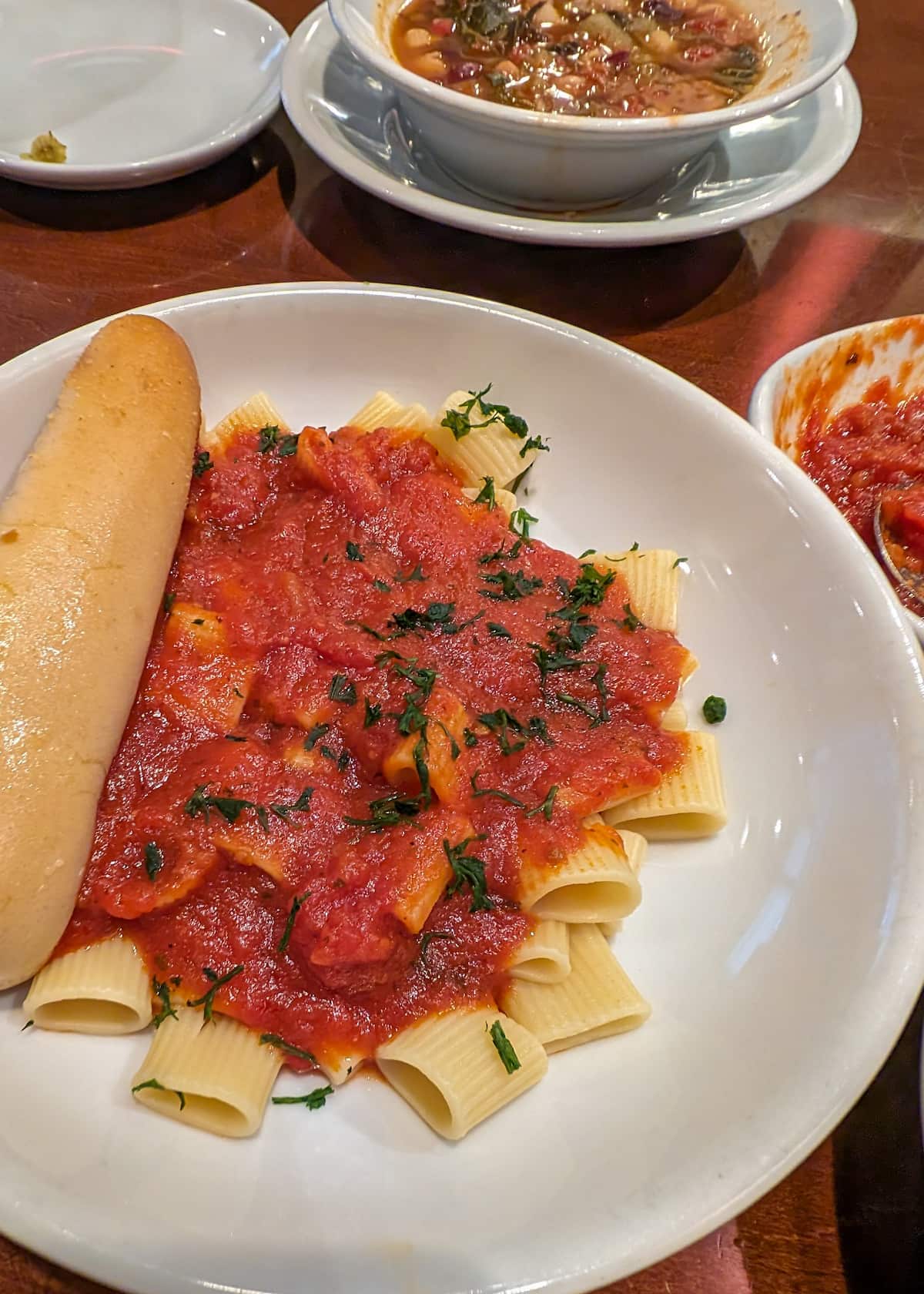 A plate of Olive Garden's pasta with tomato sauce and a breadstick.