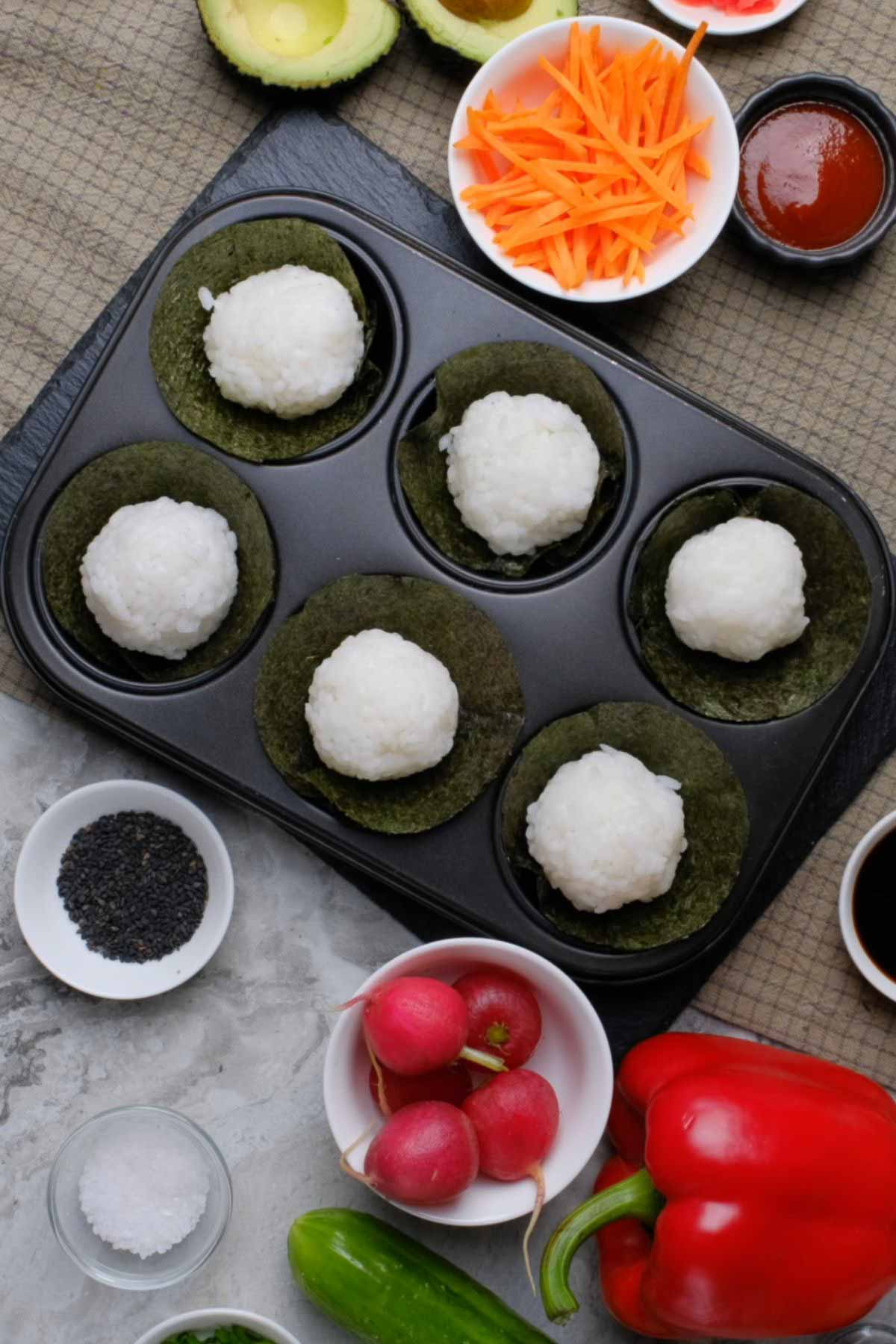 A muffin tin with sushi balls on top of circular nori sheets.