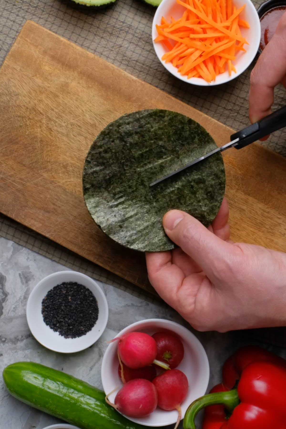 A circular piece of nori sheet being cut with scissors.