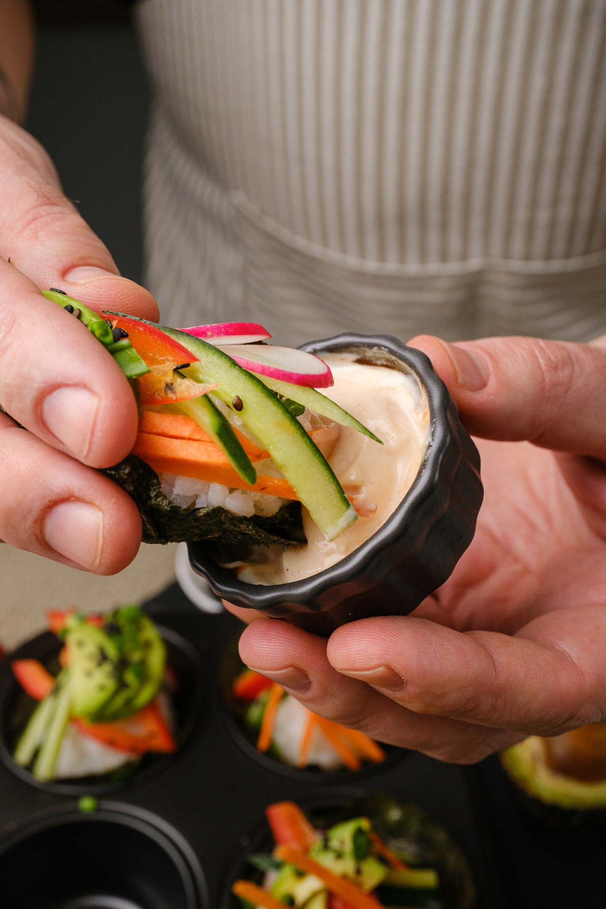 A hand dipping a sushi cupcake into sauce.