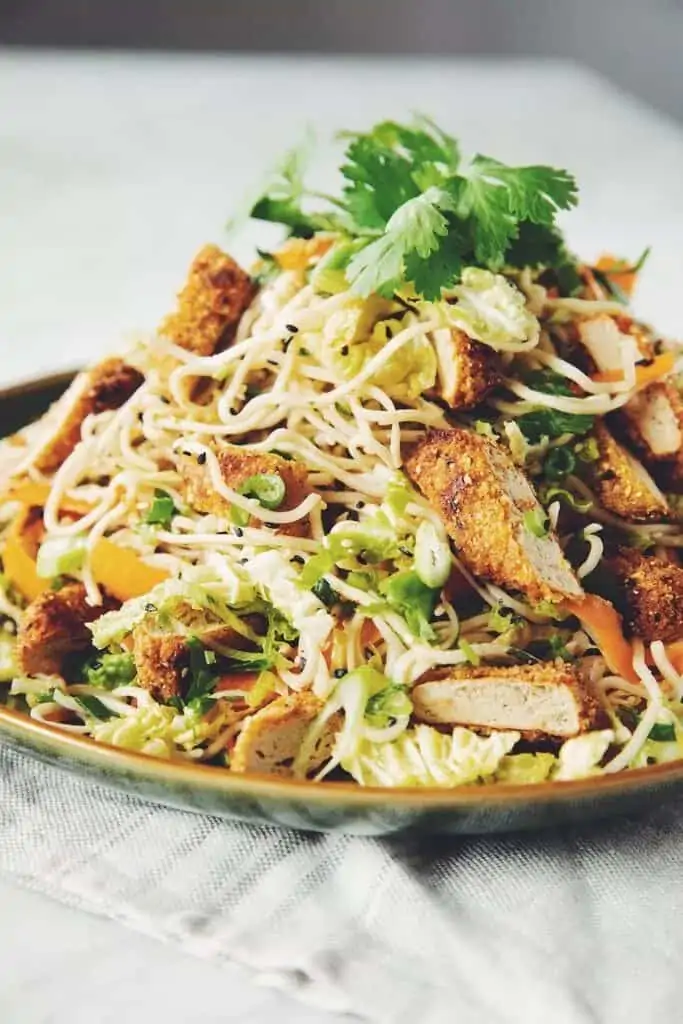 vegan asian noodle salad on a plate with crispy vegan chicken, garnished with cilantro