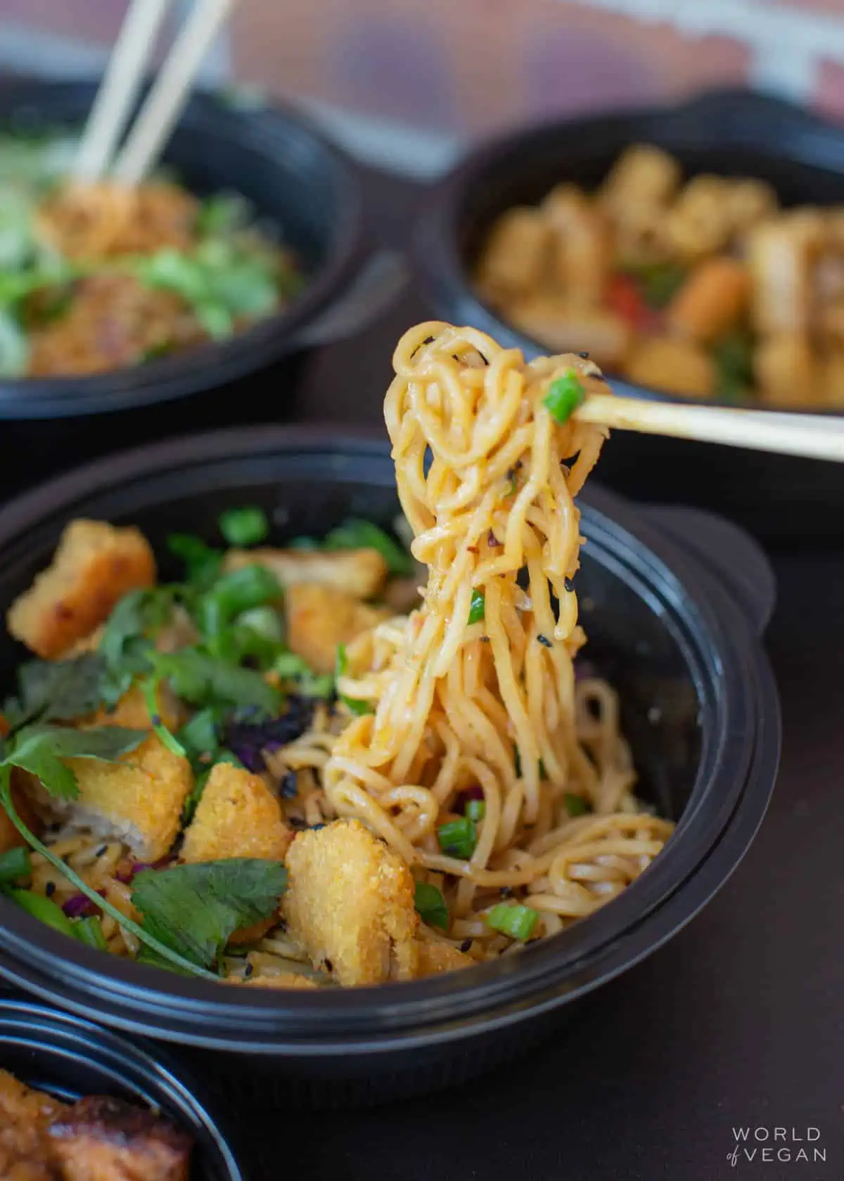 Holding up vegan Impossible Orange Chicken lo mein with chop sticks at Noodles and Company