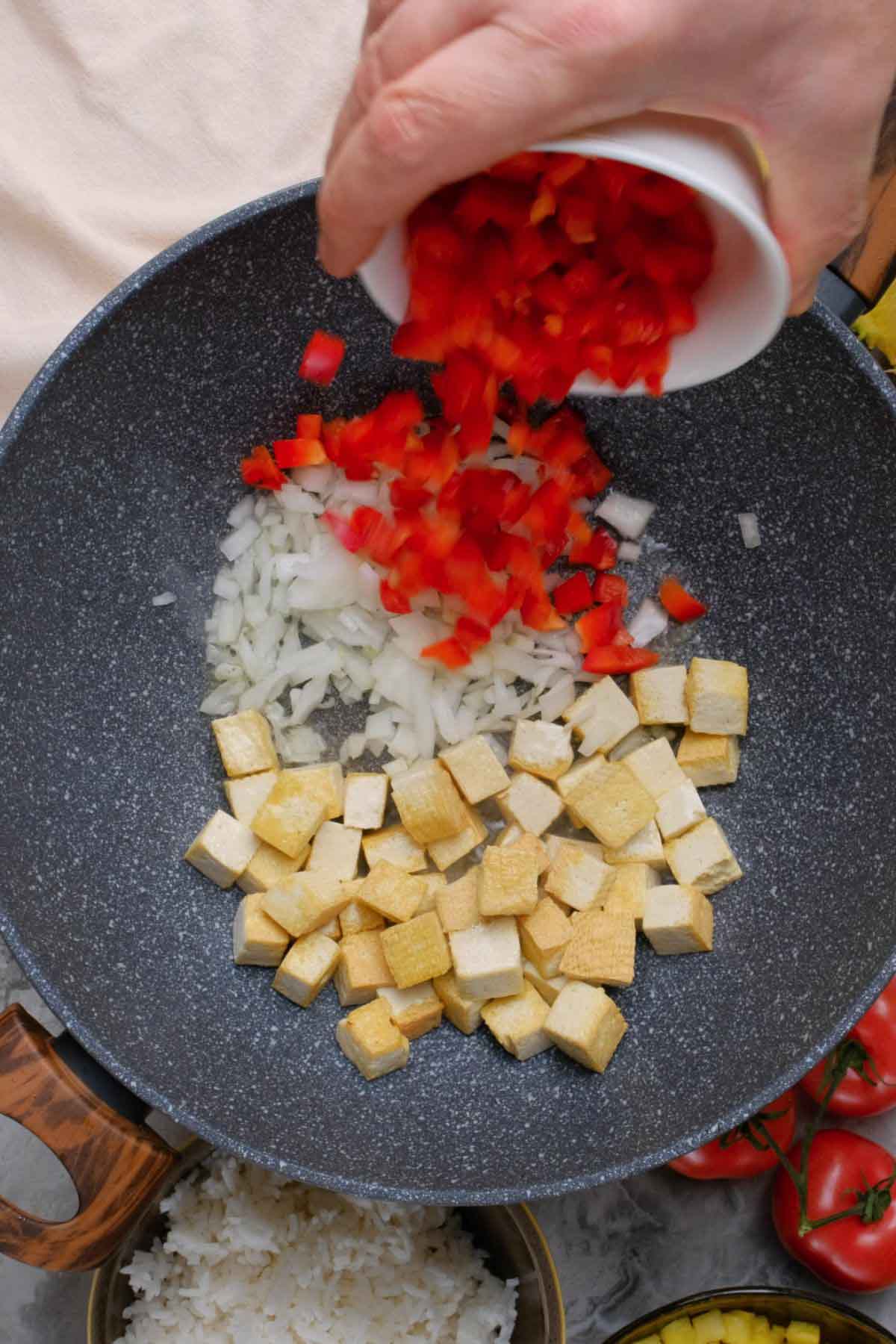 Red pepper being added to a skillet with tofu cubes and onions.