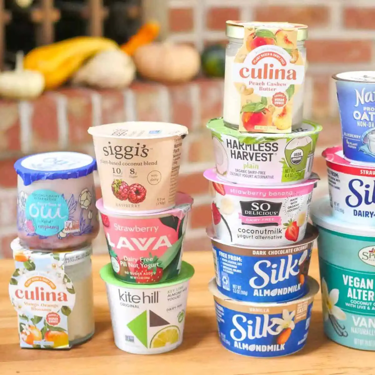 16 vegan yogurt brands in their containers stacked up on a table.