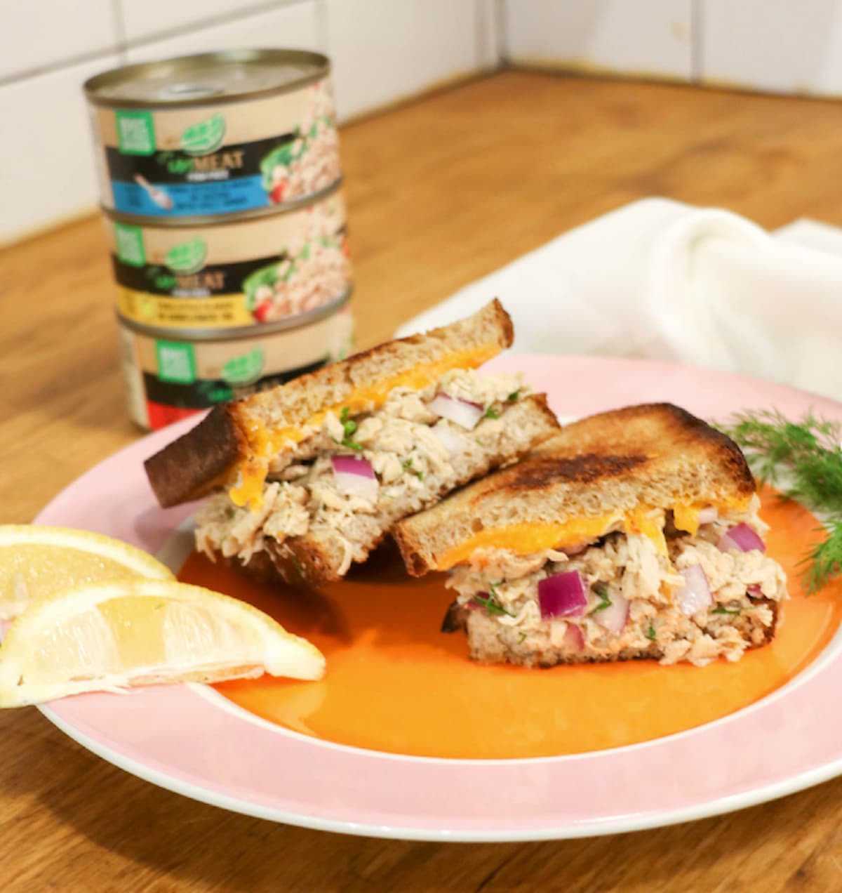 Vegan tuna melt sandwiches on a plate with unMEAT vegan tuna cans behind it.
