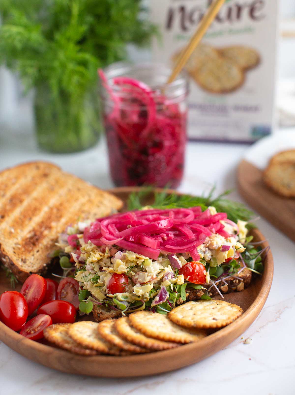 Open face sandwich piled with artichoke tuna and served with crackers and pickles. 