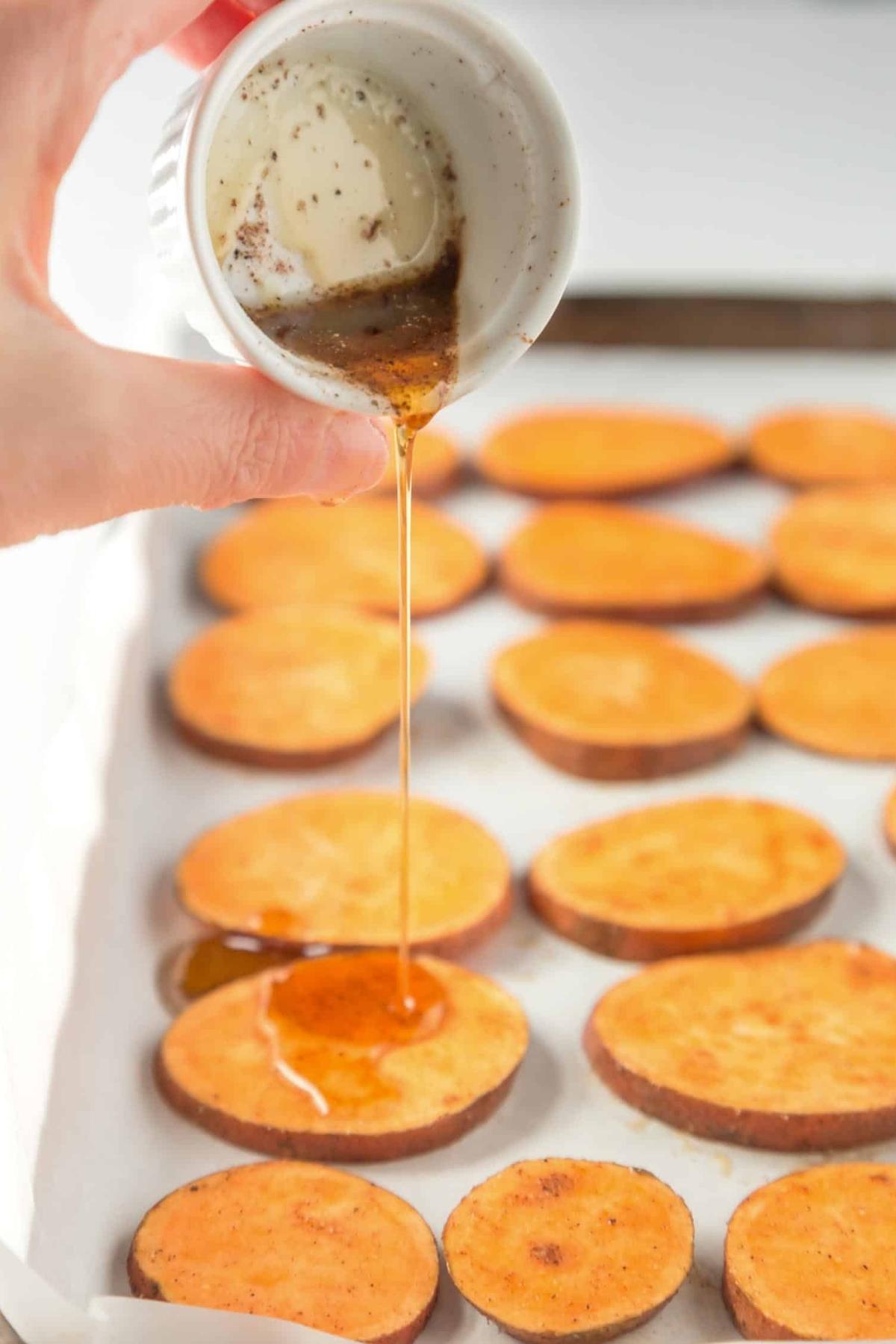 Roasted sweet pottao slices drizzled with maple syrup on a baking sheet.
