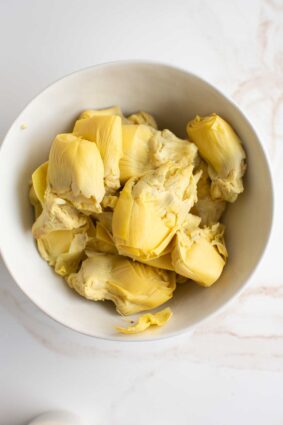 Drained artichokes from a can in a bowl. 