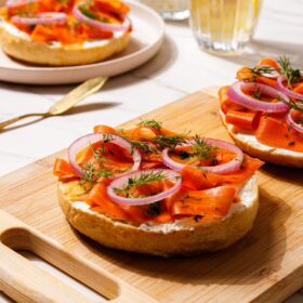 Carrot lox on top of a bagel with cream cheese, capers, and onion.