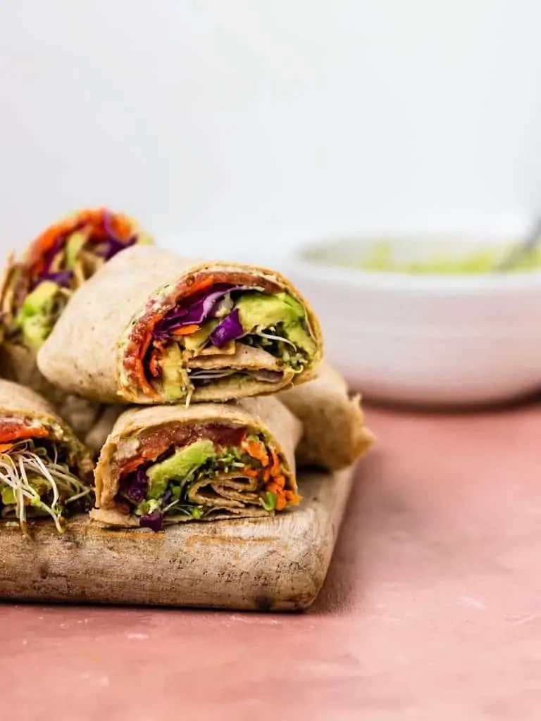 Wrap filled with edamame hummus, avocado, red cabbage, sprouts, tomatoes, and carrots