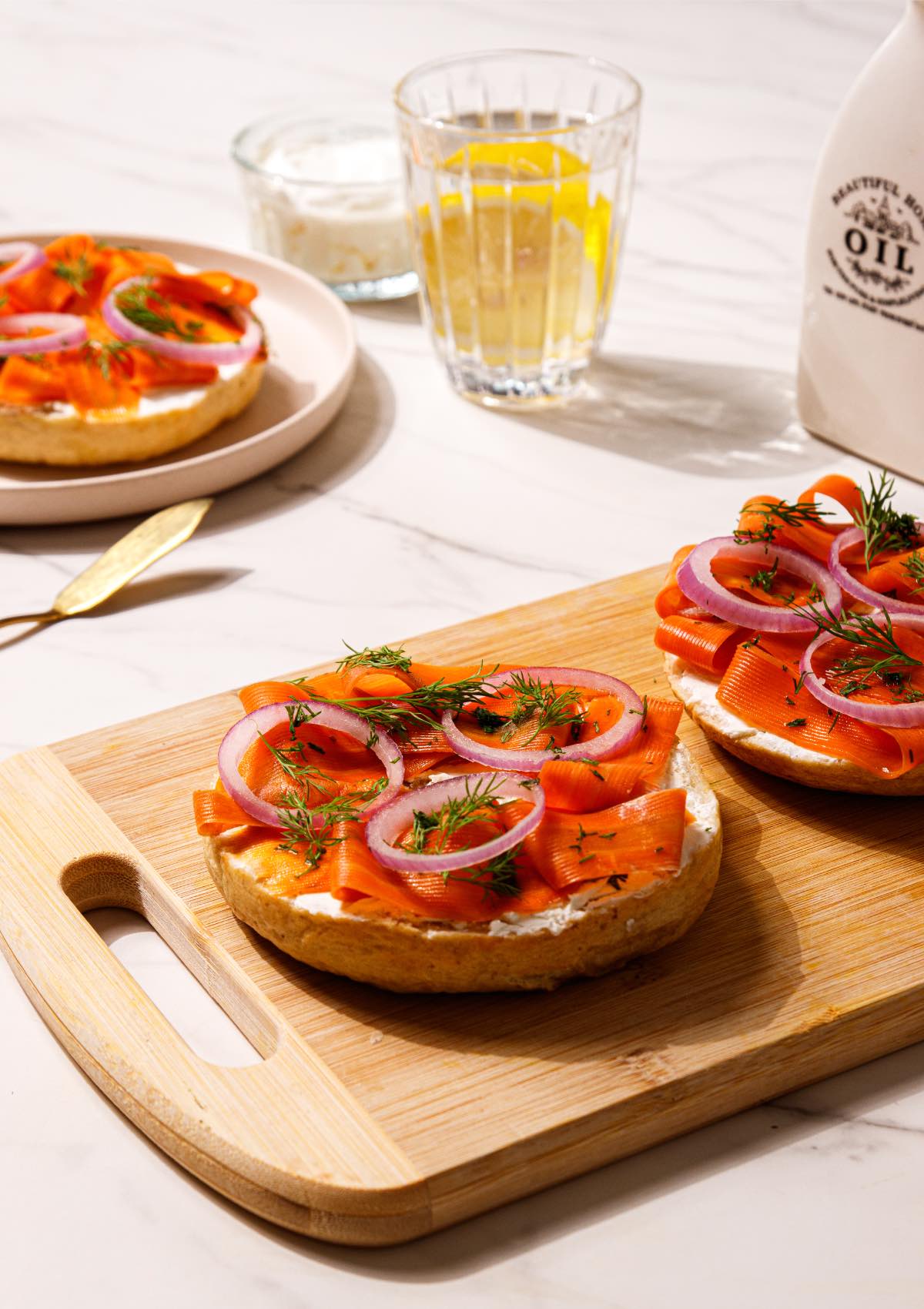 A cutting board with sliced bagels on it topped with vegan cream cheese and carrot lox.